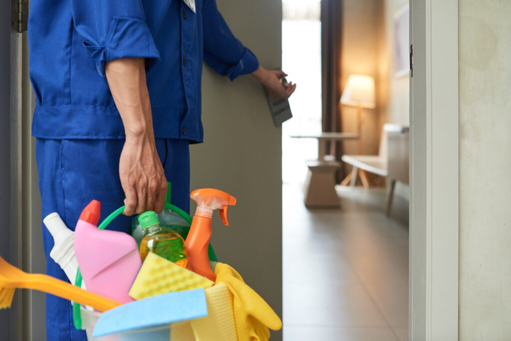 Professional home cleaner with basket of cleaning supplies entering a home to clean it.